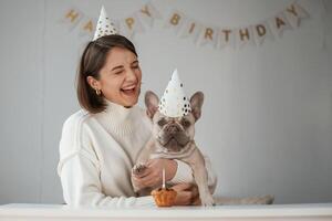 Celebration of birthday. In,, hats, and with cake. Young woman is with her pug dog at home photo