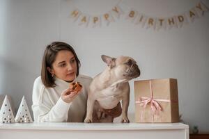 Hats, gift box and, little cake for animal who have birthday party. Young woman is with her pug dog at home photo