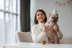 By the table, celebrating, happy ,birthday of pet. Young woman is with her pug dog at home photo
