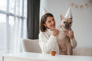 By the table,,, celebrating happy birthday of pet. Young woman is with her pug dog at home photo