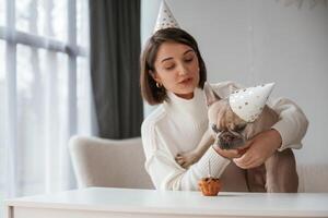 By the ,table, celebrating happy birthday of pet. Young woman is with her pug dog at home photo