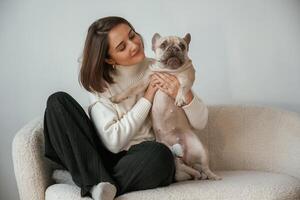Front,, view, sitting on the little sofa. Young woman is with her pug dog at home photo