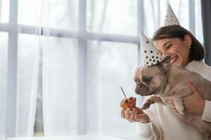 Showing, cake to pet in birthday hat, celebrating. Young woman is with her pug dog at home photo