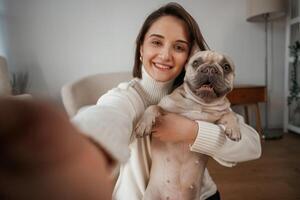 Making, selfie, smiling. Young woman is with her pug dog at home photo