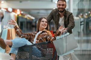 Fun in the mall, riding the shopping cart. Young couple are in supermarket together photo