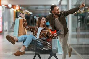 Fun in the mall, riding the,, shopping cart. Young couple are in supermarket together photo
