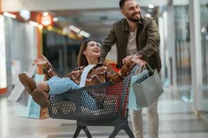 Riding ,in a shopping cart. Young couple are in supermarket together photo