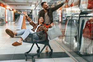 Having fun,, riding in the cart. Young couple are in supermarket together photo