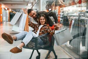 Having, fun, riding in the cart. Young couple are in supermarket together photo