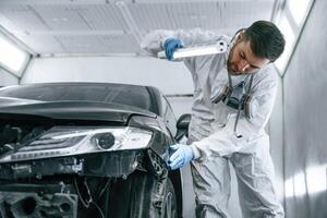 Front view. Garage worker ,is,, holding lighting and checking surface of the car photo