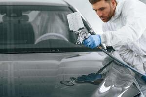 Man is painting a car by using spray guy. photo