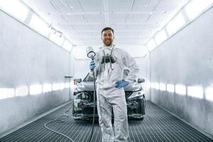 Man is standing and holding ,spray, gun with paint for automobile photo