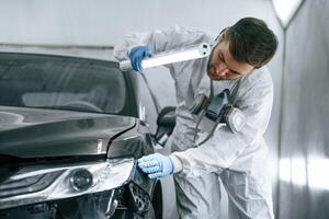 Front view.,, Garage worker is holding lighting and checking surface of the car photo