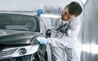 Front view. Garage worker, is ,holding lighting and checking surface of the car photo