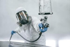 In protective mask and wear. Close ,,up, view of man that is painting a car by using spray guy photo