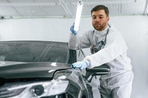 Front, view. Garage worker, is holding lighting and checking surface of the car photo