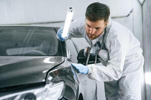 Front part of the automobile.,, Garage worker is holding lighting and checking surface of the car photo