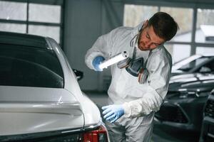 Rear part of automobile,. Garage worker is holding lighting and checking surface of the car photo