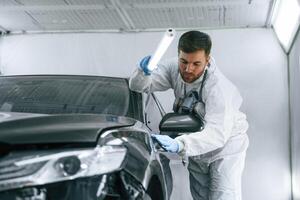 Front view... Garage worker is holding lighting and checking surface of the car photo