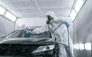 White protective wear. Man is painting, a car by using spray guy photo