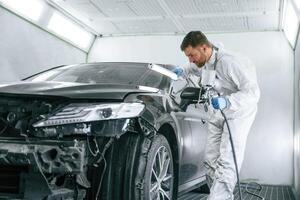 Professional worker. Man is ,,painting a car by using spray guy photo