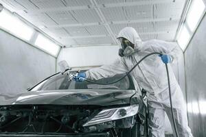 White protective wear. Man is painting a, car by using spray guy photo