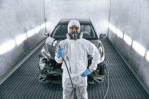 Customer service. Man, is ,standing and holding spray gun with paint for automobile photo