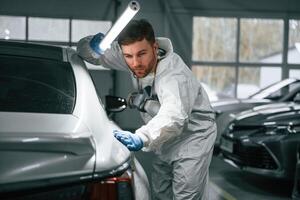 Rear part of automobile. Garage ,,worker is holding lighting and checking surface of the car photo