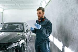 Reading information. Car painter ,is standing in the garage with documents in hands photo
