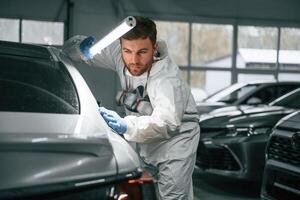 Rear ,part, of automobile. Garage worker is holding lighting and checking surface of the car photo