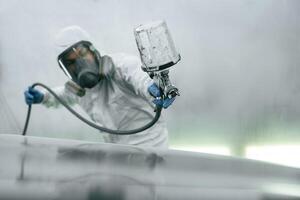 In protective mask and ,,wear. Close up view of man that is painting a car by using spray guy photo
