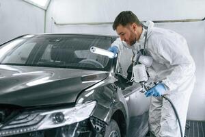 By help of lighting equipment... Man is painting a car by using spray guy photo