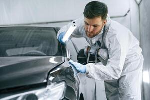 Fron,t part of the automobile. Garage worker is holding lighting and checking surface of the car photo