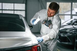 Rear, part of automobile. Garage worker is holding lighting and checking surface of the car photo