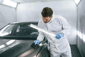 Front part, of, the automobile. Garage worker is holding lighting and checking surface of the car photo