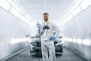 Bright artificial ,lighting. Man is standing and holding spray gun with paint for automobile photo