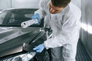 Choosin,g right, color. Garage worker is holding lighting and checking surface of the car photo