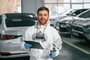 Positive facial expression.,, Car painter is standing in the garage with documents in hands photo