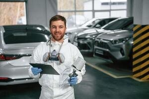 Positive facial,, expression. Car painter is standing in the garage with documents in hands photo