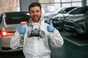Standing, in the garage with cars. Portrait of professional painter with mask photo