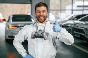 Standing, in ,the garage with cars. Portrait of professional painter with mask photo