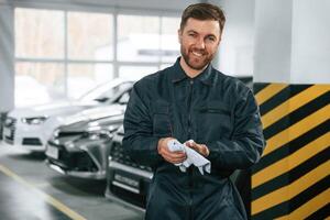 Wiping ,hands. Repairman in, uniform is standing in the garage with cars photo