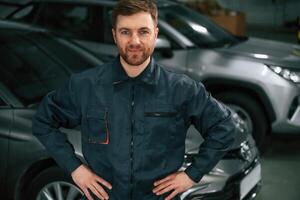 Handsome friendly ,guy. Repairman in uniform is standing in the garage with cars photo