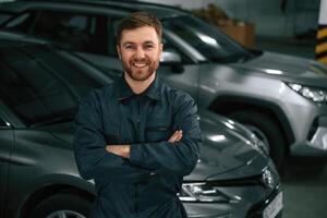 Repairman ,in ,,uniform is standing in the garage with cars photo
