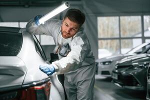 Searching for, imperfections.. Garage worker is holding lighting and checking surface of the car photo