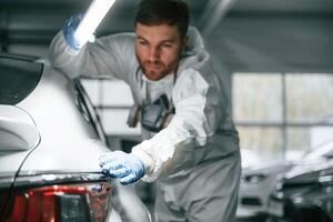 Searching for, imperfections. Garage worker is holding lighting and checking surface of the car photo