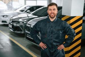 Repairman, in uniform is standing in the garage with cars photo