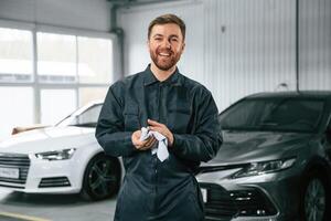 Handsome,, friendly guy. Repairman in uniform is standing in the garage with cars photo