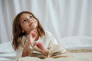 Lying, down on the bed with book. Cute little girl is at home photo
