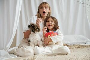 Watching movie, with, popcorn and dog. Mother with daughter are at home together photo